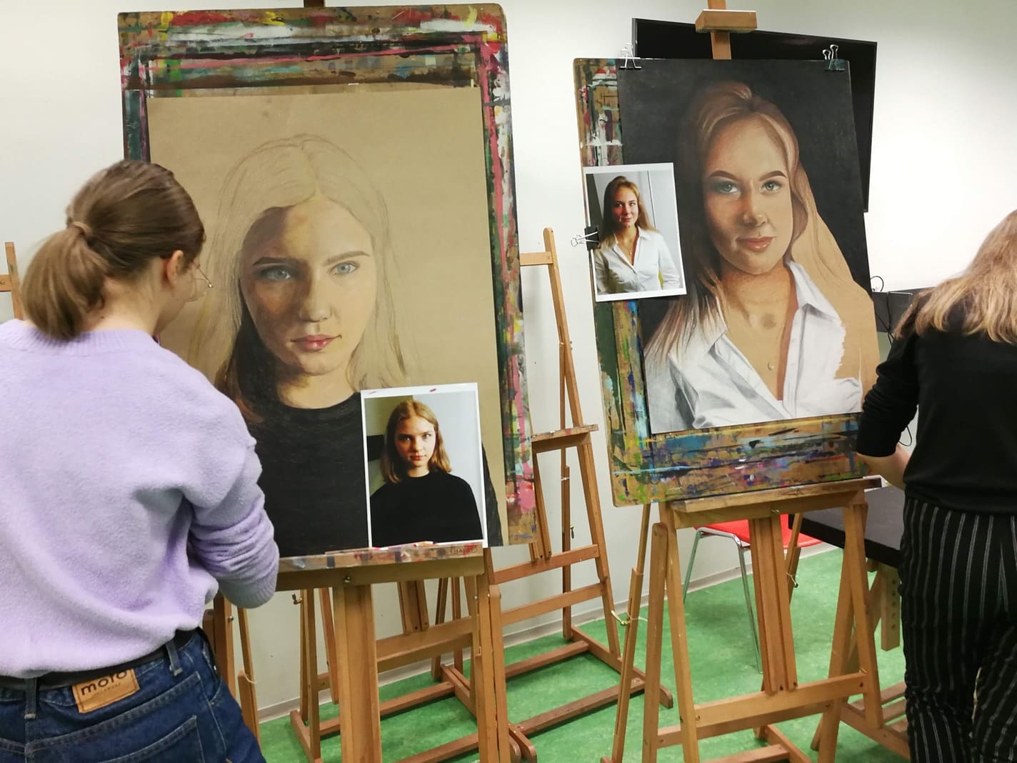Fotol on kaks tüdrukut, kes joonistavad värvipliiatsitega hüperrealistlikke autoportreesid
